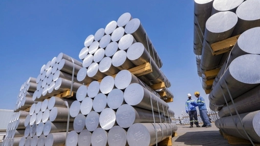 Stacked aluminum billets on pallets at an outdoor yard with two workers in safety gear inspecting the load