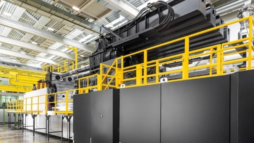 Heavy black industrial machine with yellow safety barriers and an overhead crane in a manufacturing facility