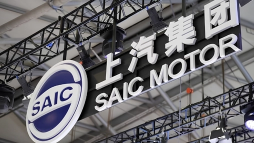 An illuminated corporate sign with Chinese and English lettering suspended from exhibition hall rigging