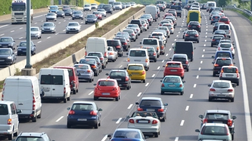 Rows of cars, vans, and trucks moving slowly across several lanes on a divided highway with guardrails