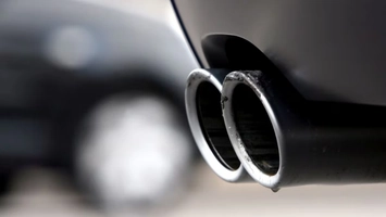 Close-up of twin chrome exhaust pipes on a dark vehicle undercarriage, highlighting vehicle emission output